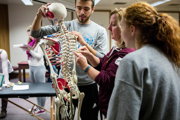 Students and professor looking at skeleton in classroom